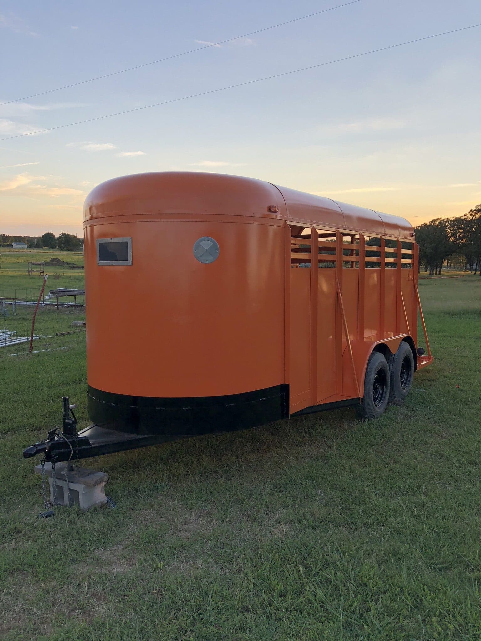 A freshly painted orange livestock trailer standing in a field at dusk